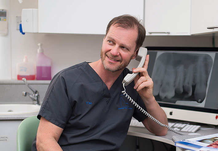 Advice Appetiser A dentist wearing dark grey scrubs is on the phone at a desk in a dental surgery